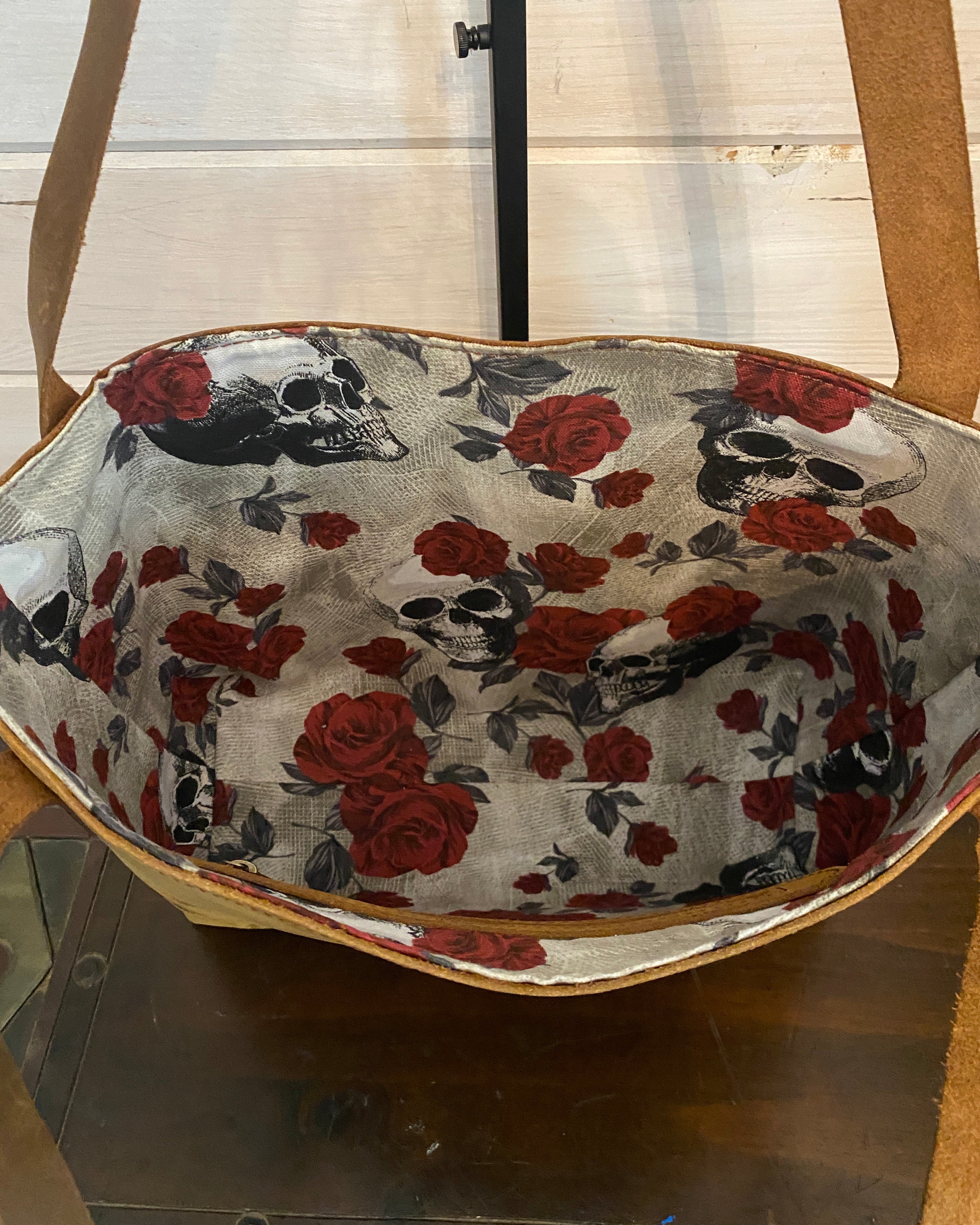 A close-up of a fabric product, likely a hat or bag, featuring a printed pattern of red roses and black-and-white skulls on a light beige background.