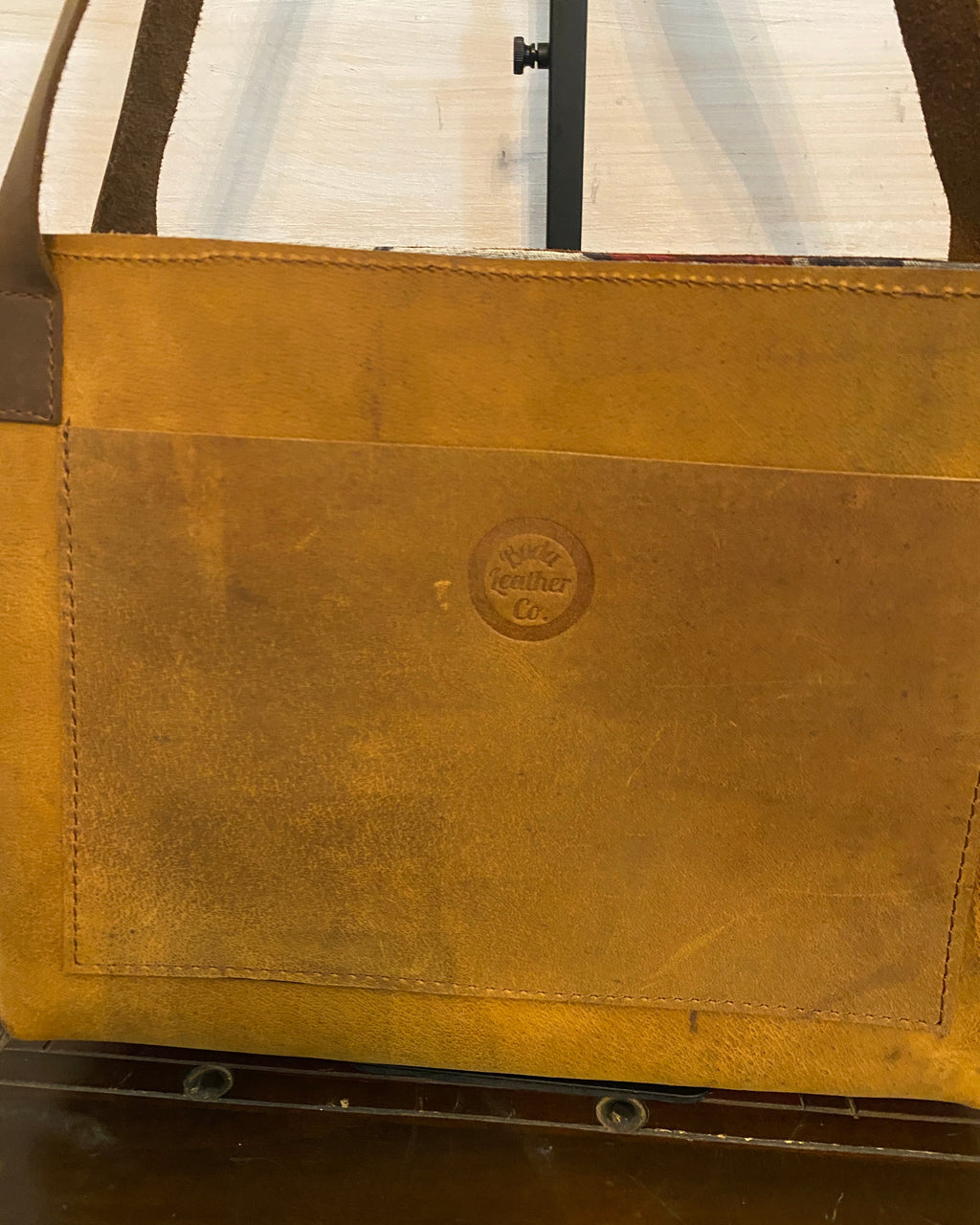 A close-up of a brown leather or faux-leather cover with visible stitching and a circular embossed logo in the center, shown against a dark and light background.