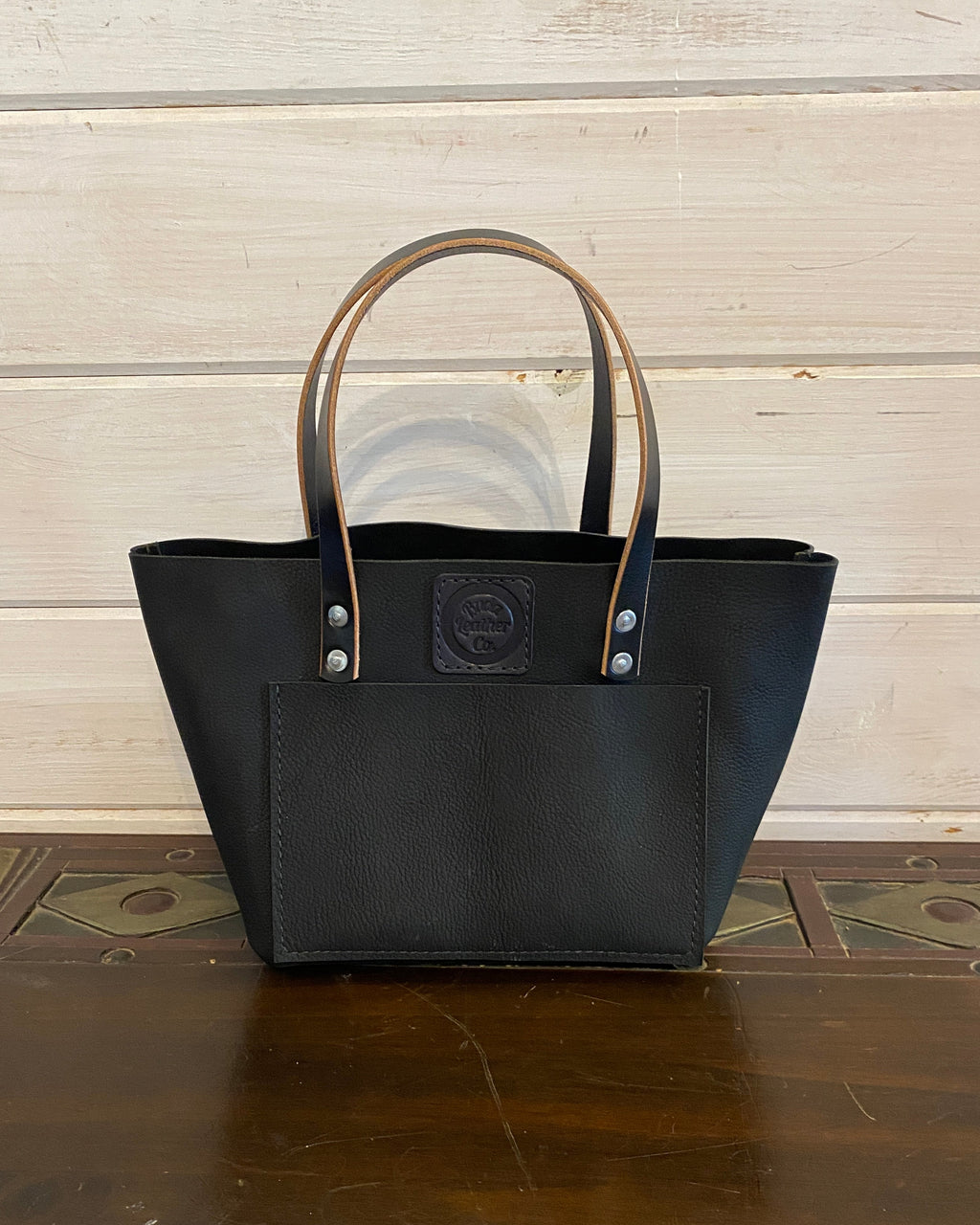 Buda Leather medium tote made from pebbled black top-grain leather with front pocket, stamped logo patch, and silver hardware.