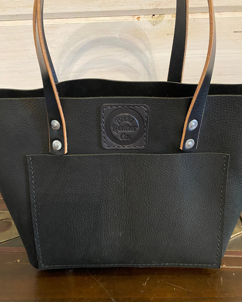 Buda Leather medium tote made from pebbled black top-grain leather with front pocket, stamped logo patch, and silver hardware.